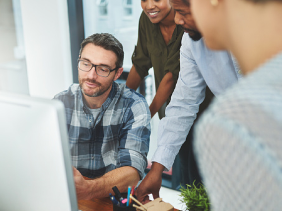 Several people looking at a laptop and talking. 